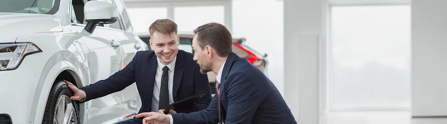 two guys in suits bent down looking at the tires of a car