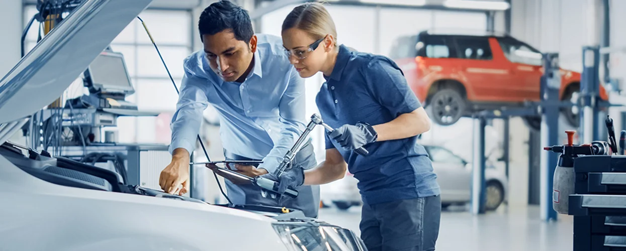 Two people engaged in automotive work inside a garage, utilizing various tools to fix the car.