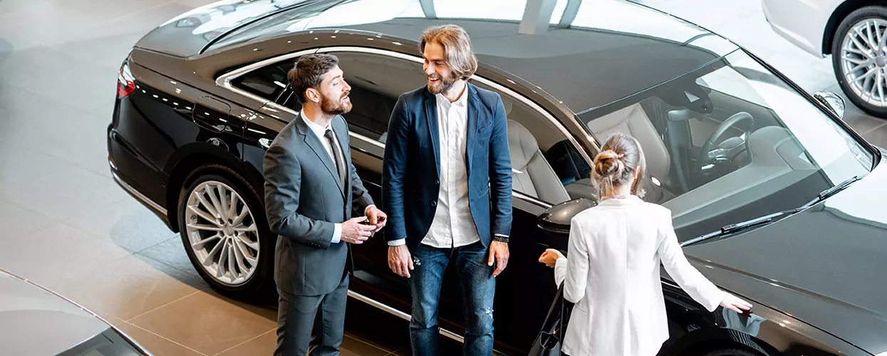 Car dealership sales consultant assisting customers while exploring a luxury sedan in a modern showroom