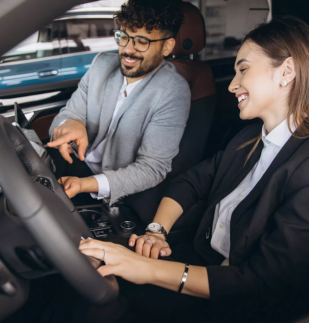 Two people sitting inside a new Kia at a car dealership