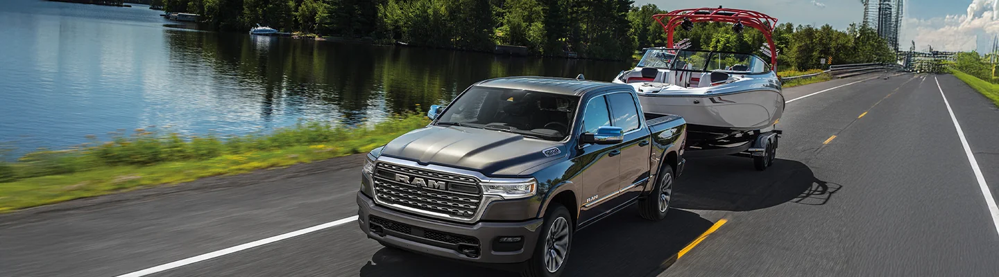 RAM truck towing a boat down the road with a lake next to the road