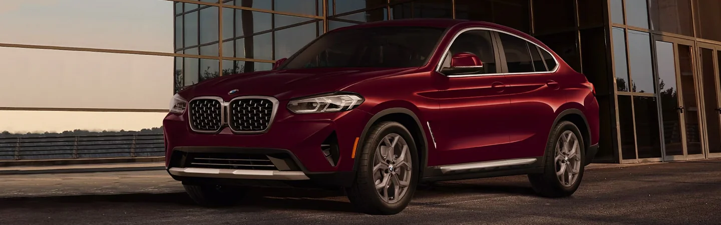 A parked red 2024 BMW X4 in front of a building
