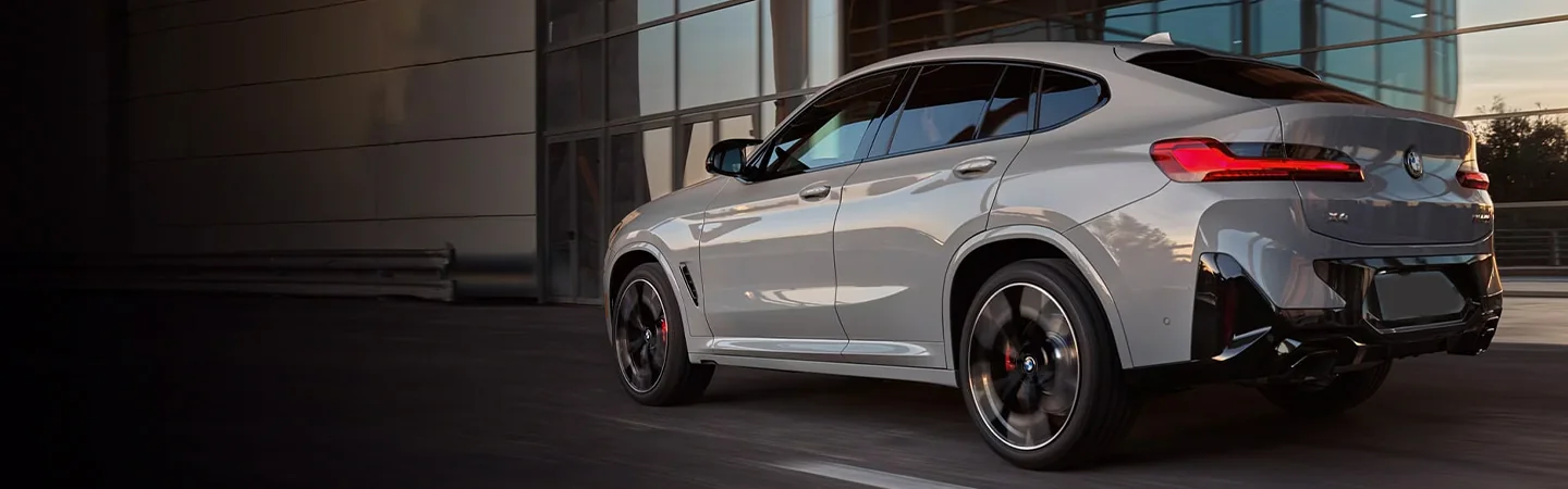 Back side view of a gray 2024 BMW X4 driving in the city