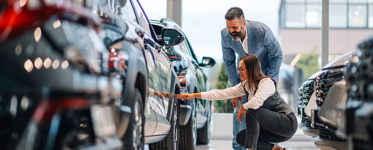 Car dealership sales consultant helping a customer compare vehicles and explore features in a modern showroom