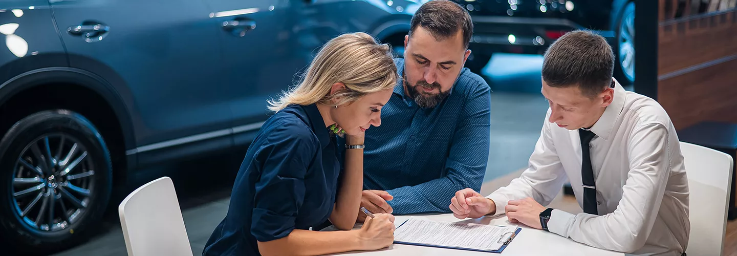 Three people sitting at a table in a dealership