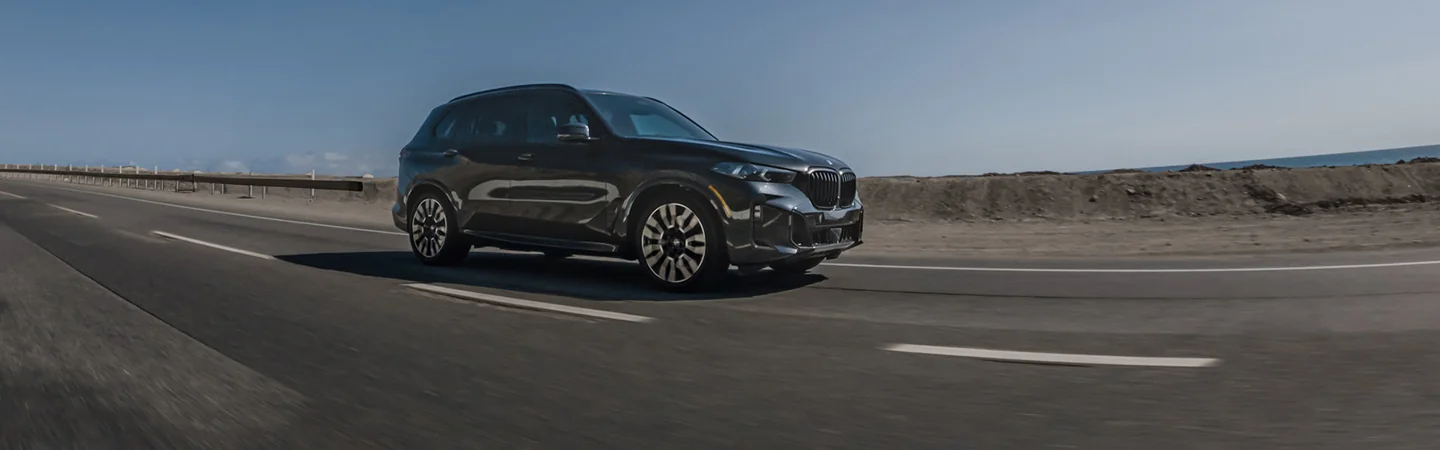 Side view of a black 2026 BMW X5 driving on a road in the middle of nowhere