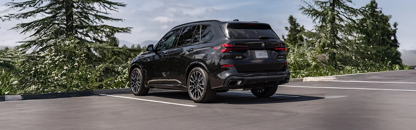 Back side view of a 2026 BMW X5 parked by the woods