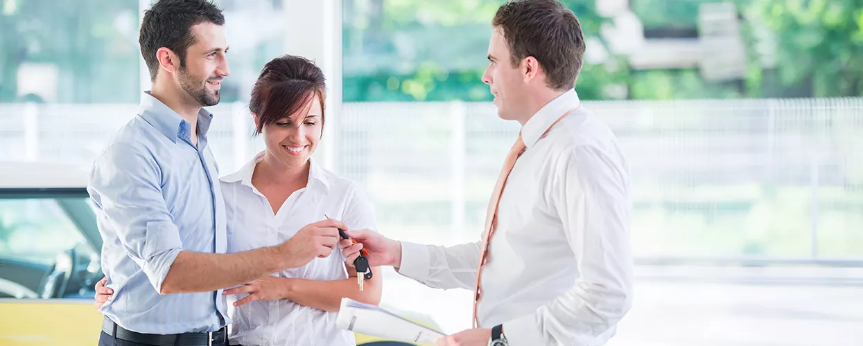 Car salesman handing a couple a new set of car keys