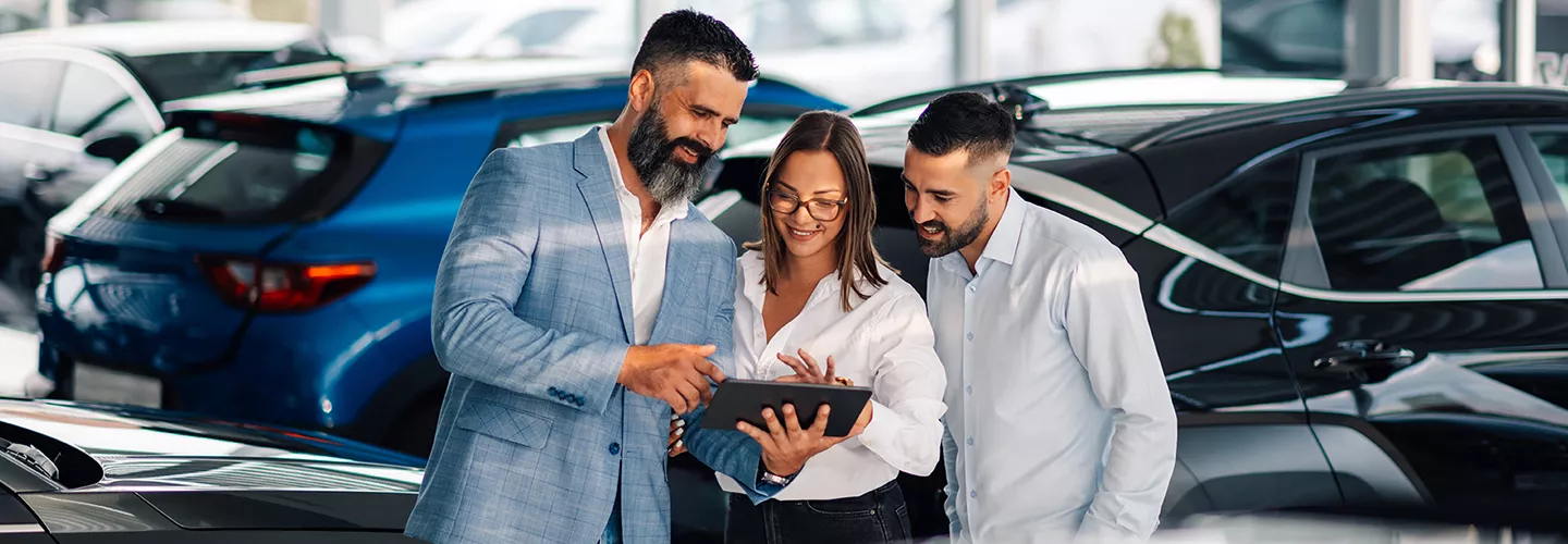 Three people looking at an ipad in a dealership