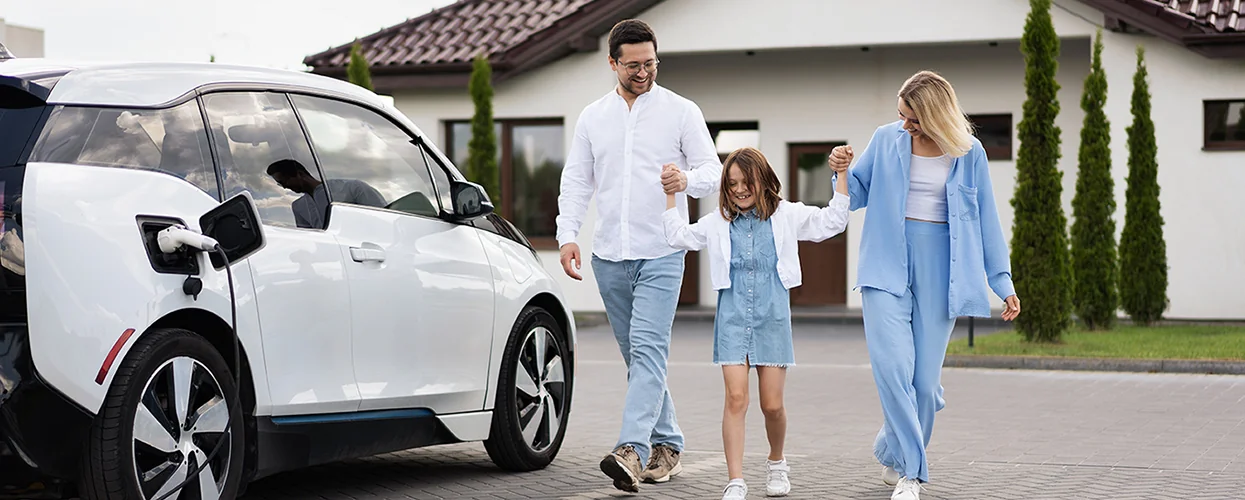 A family walking over to there white EV SUV charging in there driveway