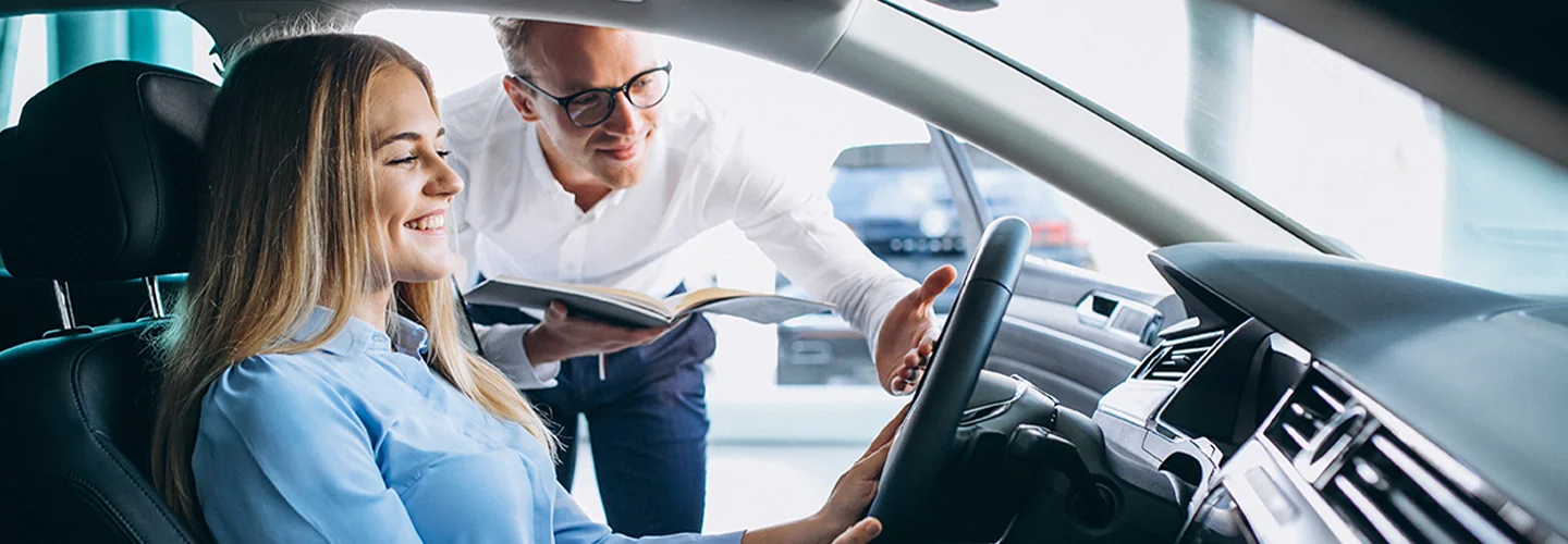 a car salesperson leaning into car driver side to show person car features