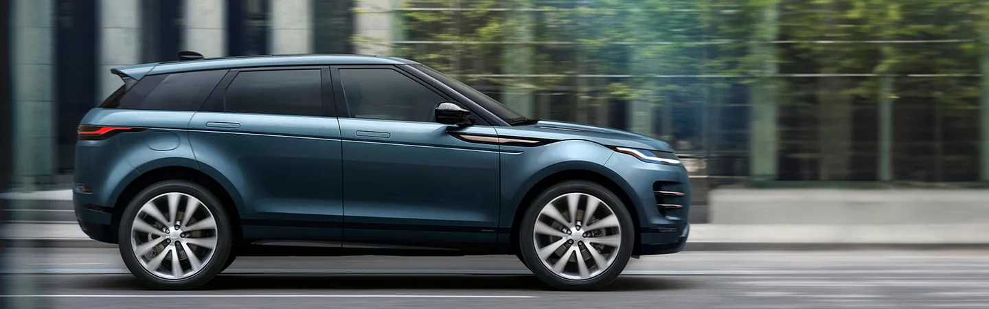 Side view of a blue 2026 Range Rover Evoque drving next to a glass building