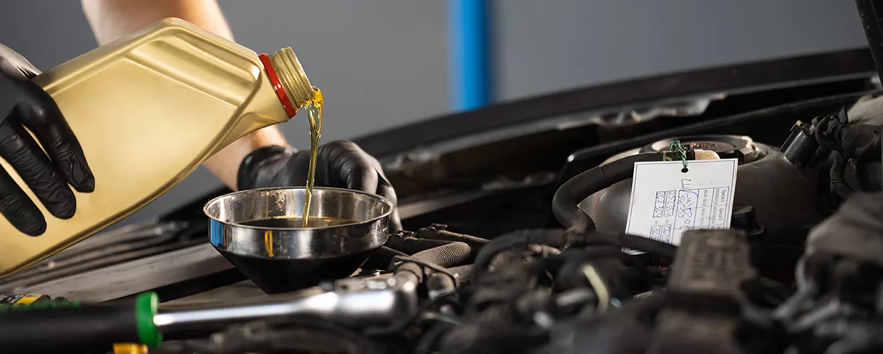 Automotive technician performing an engine oil change by adding fresh motor oil during routine vehicle maintenance service