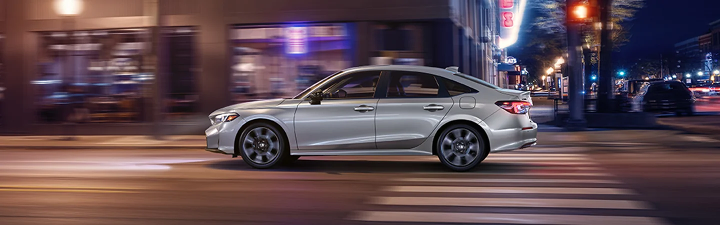 Side view of a gray 2026 Honda Civic driving in the city at night