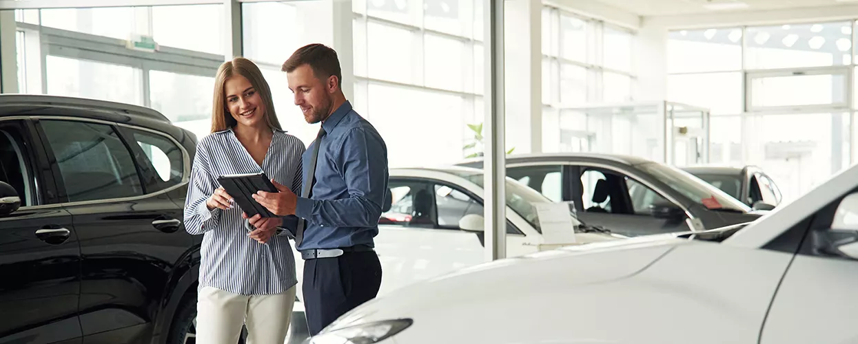 Car salesman showing a customer something on a tablet in a car dealership