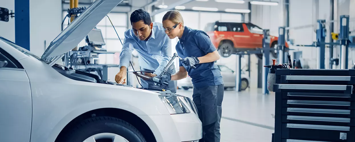 Two service mechanics working under the hood of a vehicle
