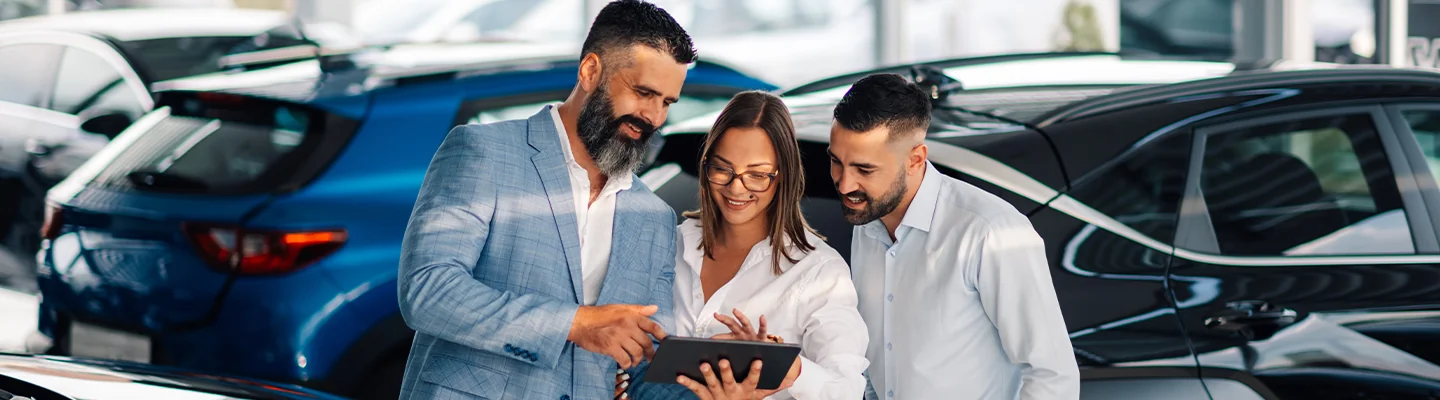 car salesperson showing used car information to a couple in the dealership showroom