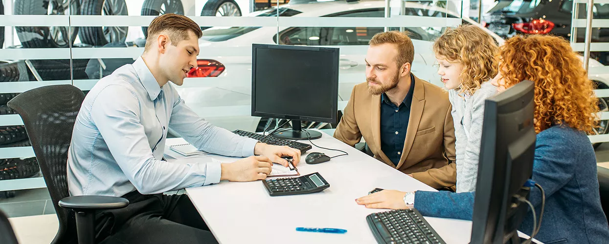 Dealership finance specialist reviewing vehicle financing and purchase options with a family in a modern automotive showroom