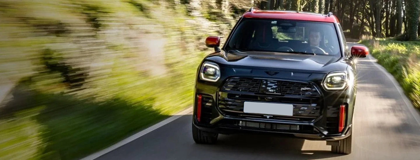 Front view of a black 2025 JCW Countryman ALL4 driving on a road