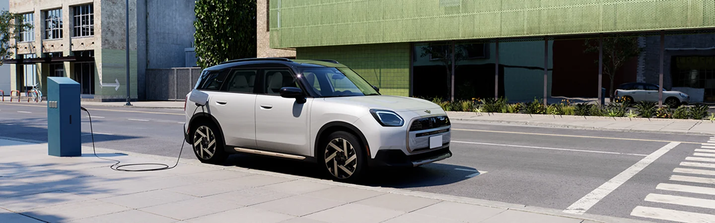 A white 2025 MINI Countryman SE ALL4 parked on a city street getting charged