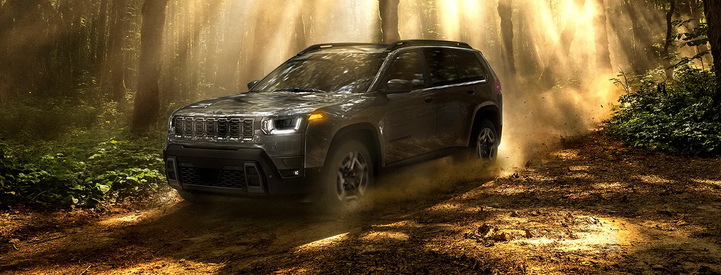 A gray 2026 Jeep Cherokee driving though the woods on a dirt trial