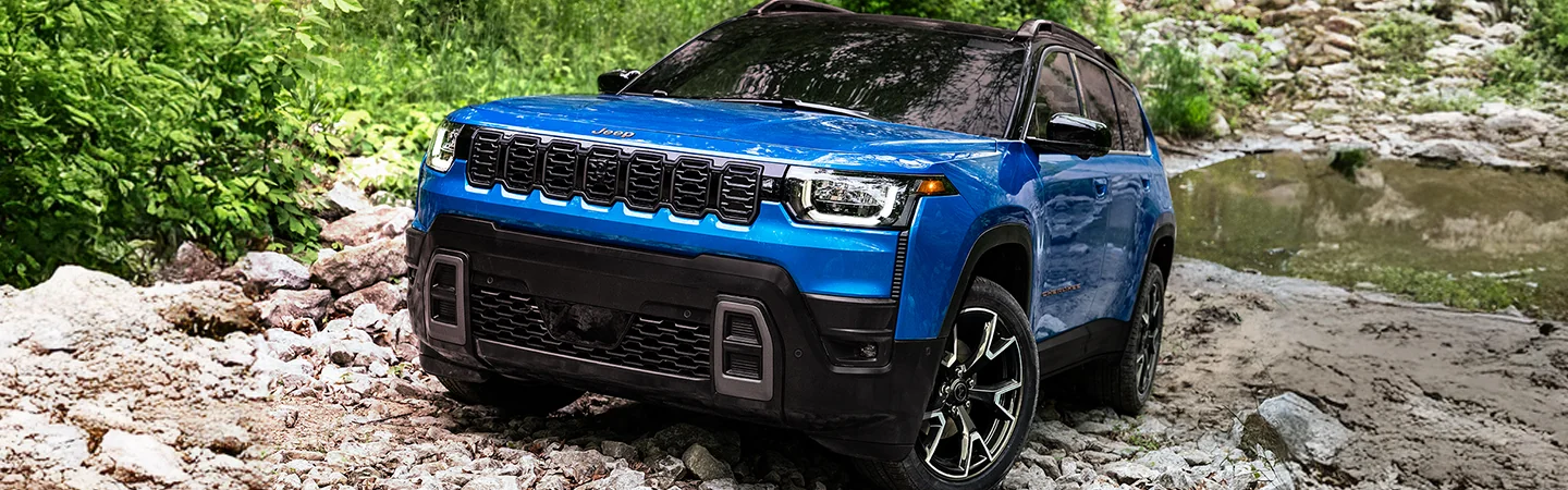 Parked blue 2026 Jeep Cherokee on some rocks by some water