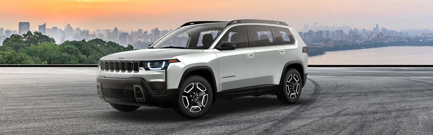 Front side view of a parked gray 2026 Jeep Cherokee with a city in the background