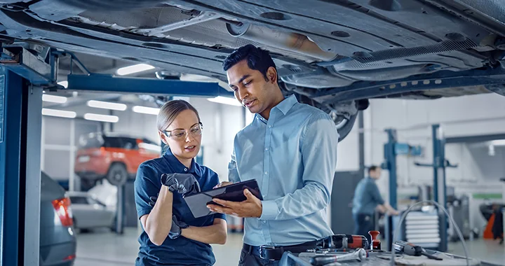 Mechanics reading a checklist under car on lift