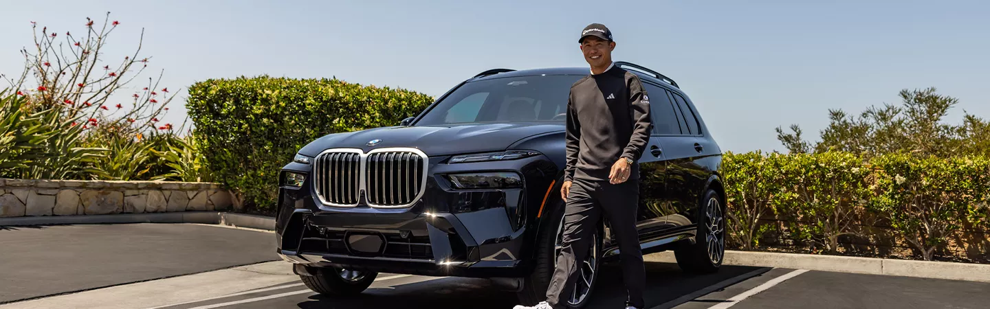 Person walking away from a 2026 BMW X7 parked in front of bushes