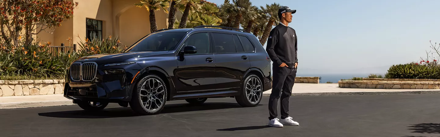 Man standing in front of a parked 2026 BMW X7 and palm trees with the ocean in the background