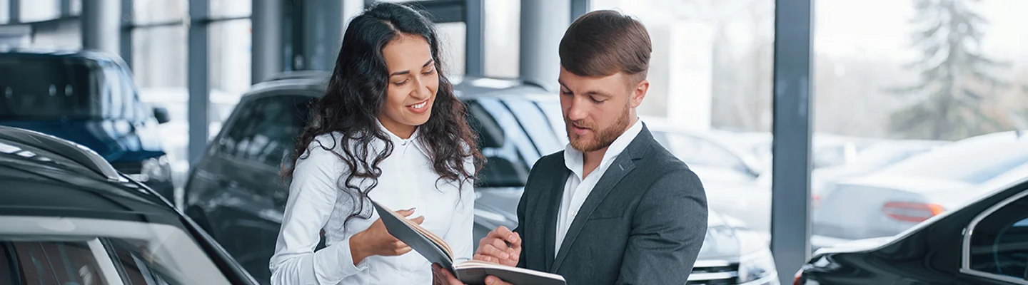 Sales person showing customerpaperwork on the new car they are looking at
