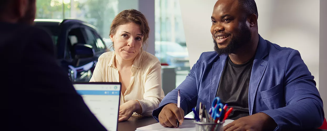 a couple in view discussing a car purchase with person back turned at a dealership