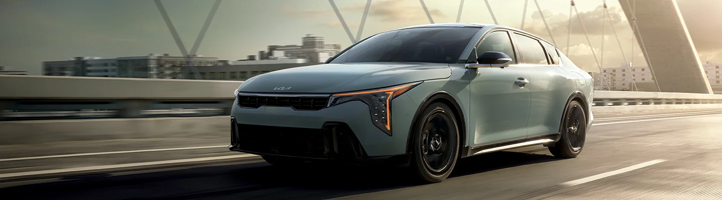 Front view of a Kia driving over a bridge in a city