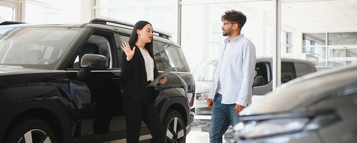 Where Can I Find Used Cars for Sale Under $25K in Ocala? in Customer discussing vehicle features with a dealership representative next to a new SUV in a car showroom