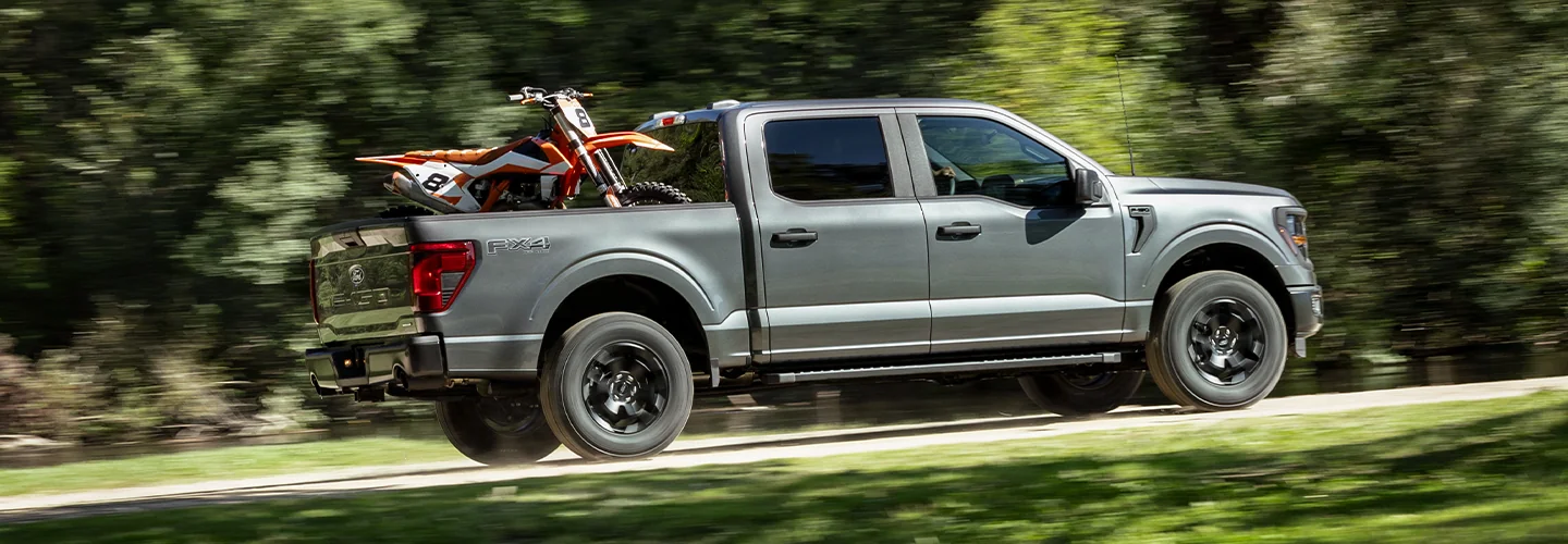 2025 Ford F 150 driving on a country road with a dirtbike in the bed