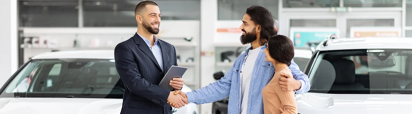 Customers shaking hands with a sales person while shopping for a used car