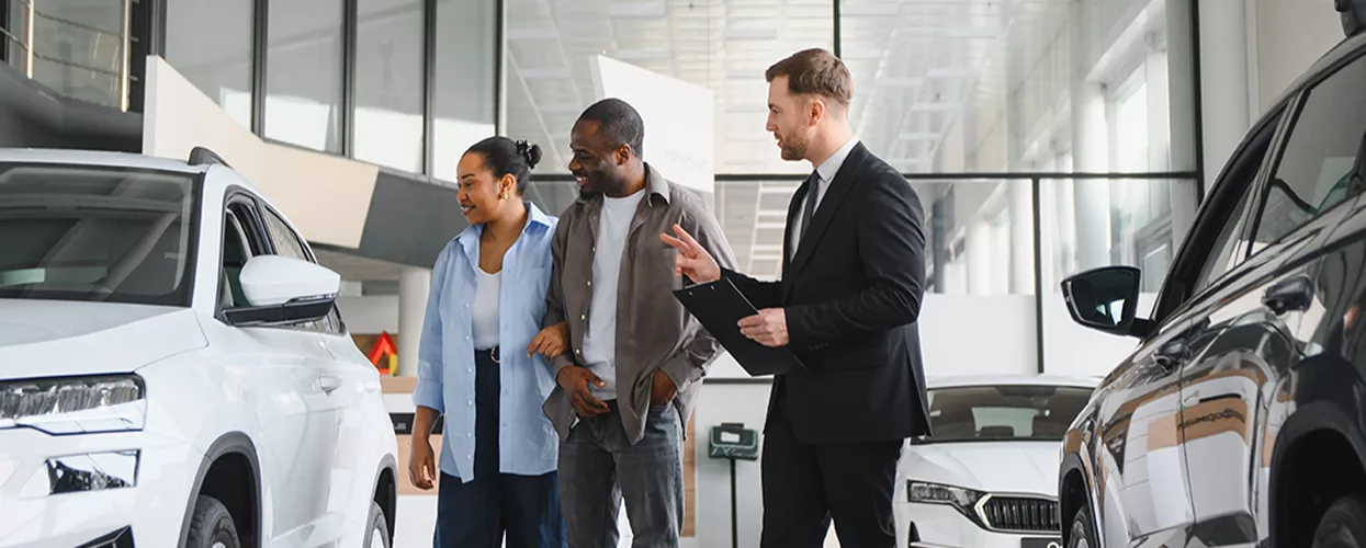 Car dealership sales consultant assisting customers as they explore SUV models in a modern showroom
