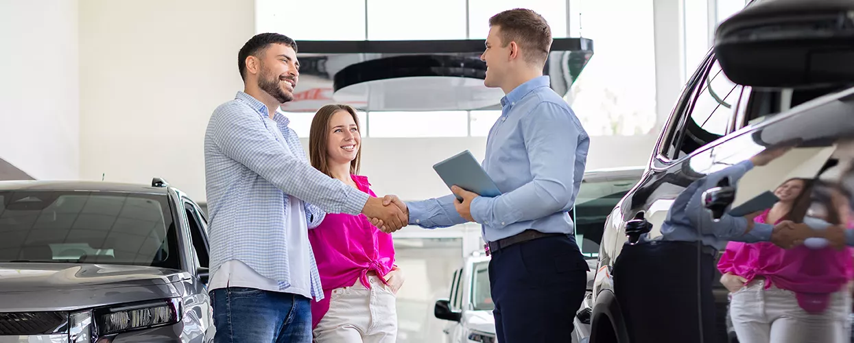 Couple shaking hands with a car salesman in a car dealership
