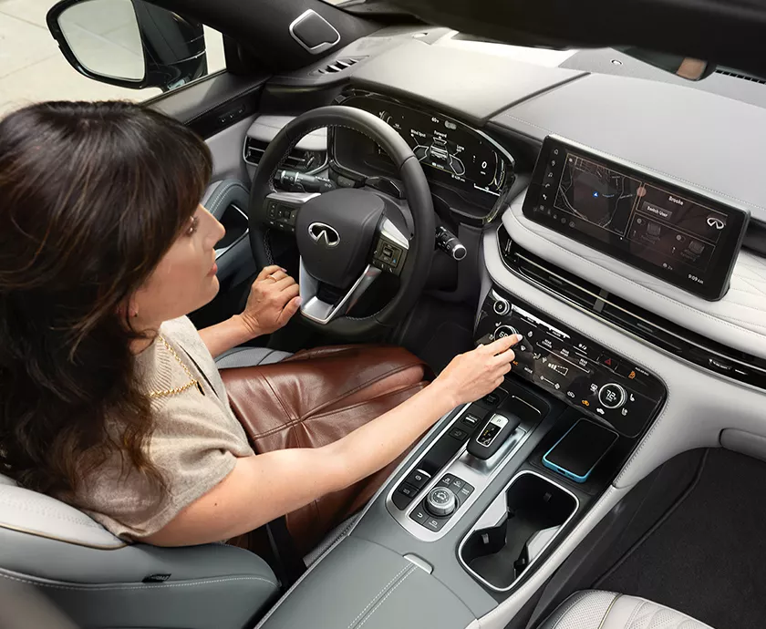 2027 INFINITI QX60 Vehicle interior showing the front seating area with driver checking out dash electronics