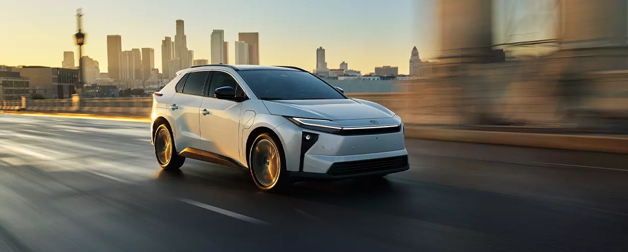 a white Toyota bZ driving in the city by sunset