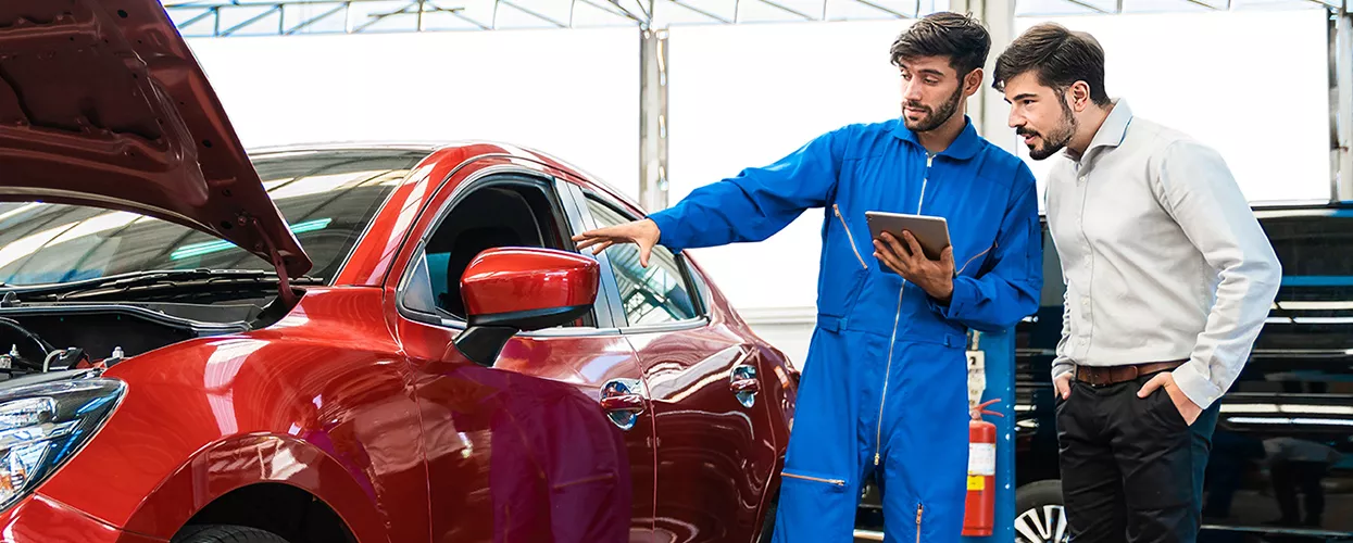 two people going over service in service bay overlooking a red car