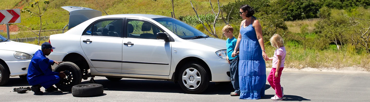 Roadside service attending to a broken down vehicle with a family standing next to it on the side of the road
