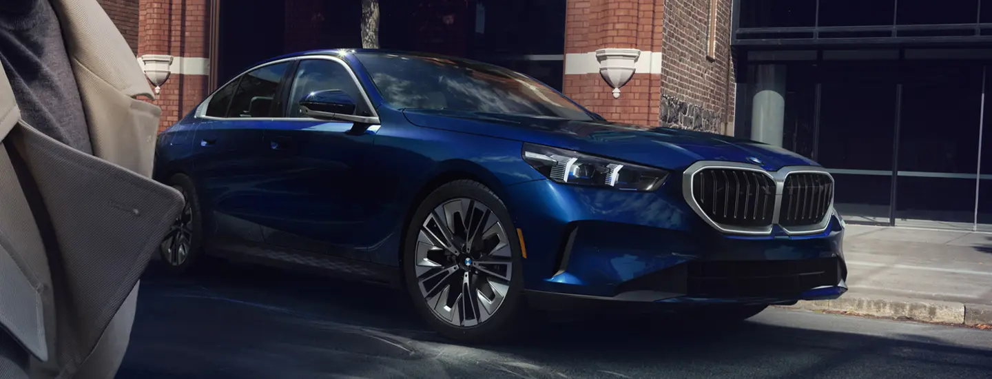 Front view of a 2025 BMW 5 Series parked by some houses