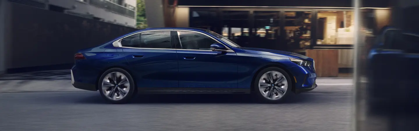 Back view of a blue 2025 BMW 5 Series driving on a road
