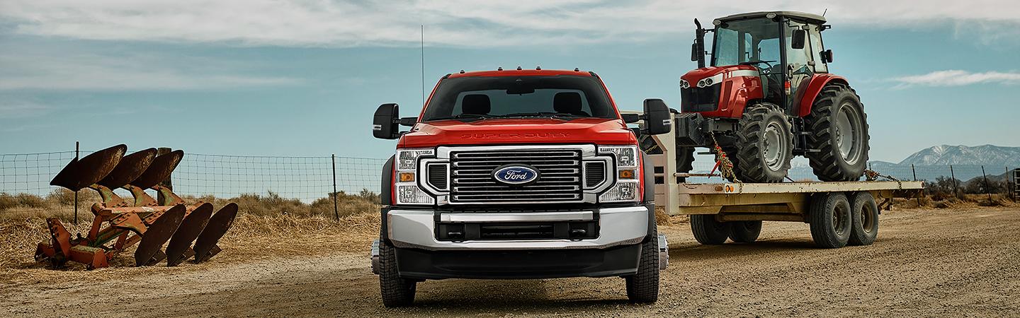 Front view of a red Ford Super Duty truck towing farm equipment