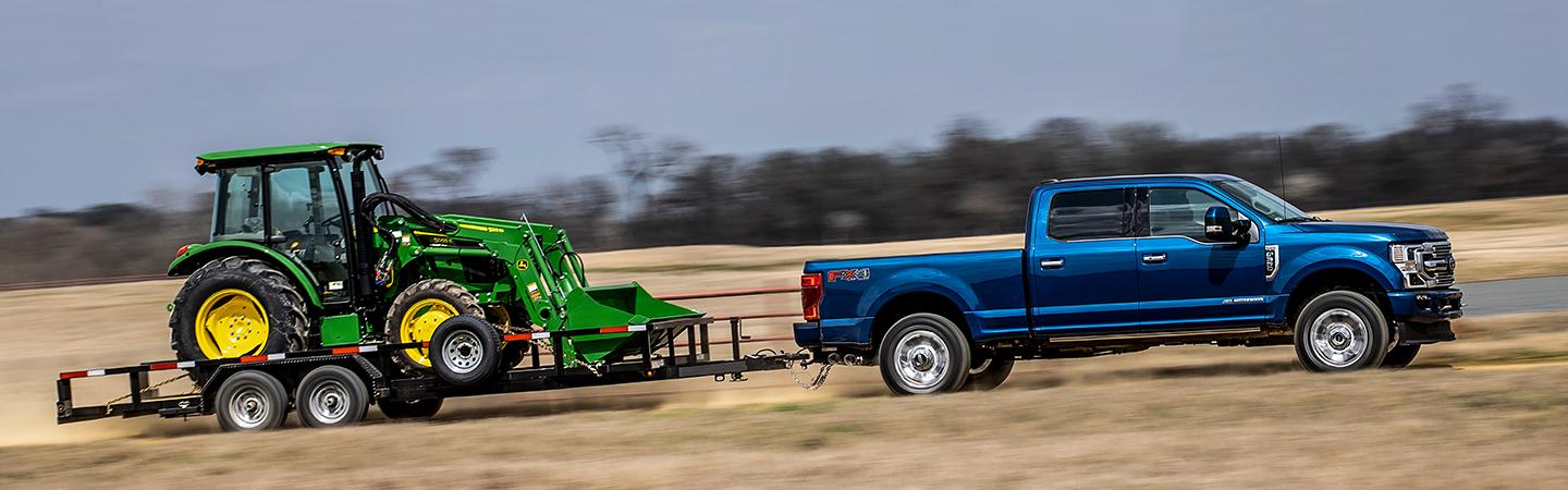 Side profile of a blue 2022 Ford Super Duty towing a tractor