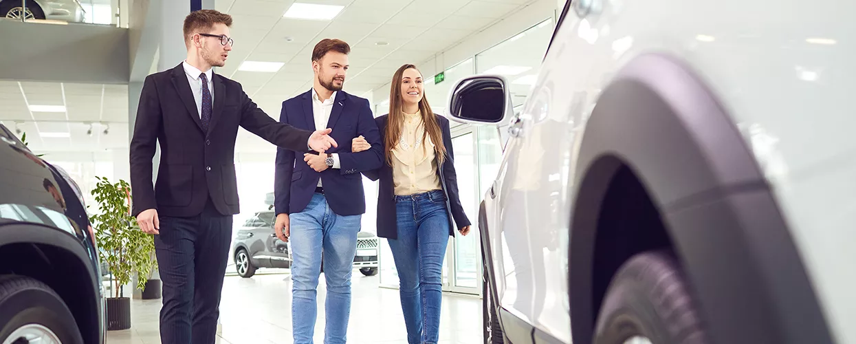 Car salesman walking through a car dealership with two customers