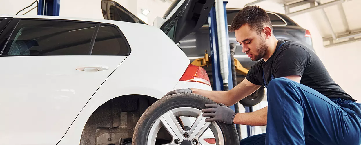 auto mechanic working on tire of car in service bay
