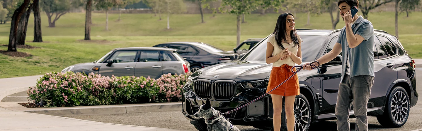 People standing talking on the phone next to a 2026 BMW X5 with their dog on a leash