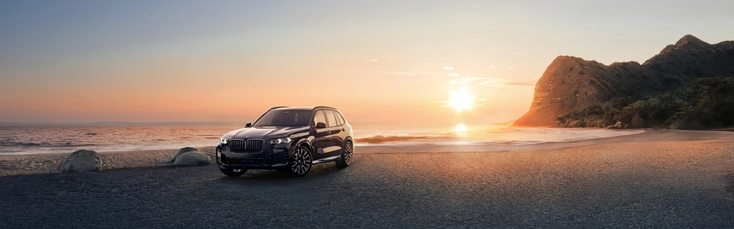 2026 BMW X5 parked on a beach with the sun setting in the background